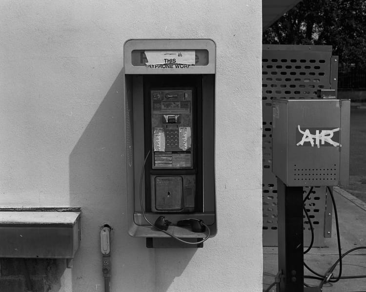An old payphone. A worn sign on the top reads "This Payphone Works" but the broken reciever suggests otherwise.