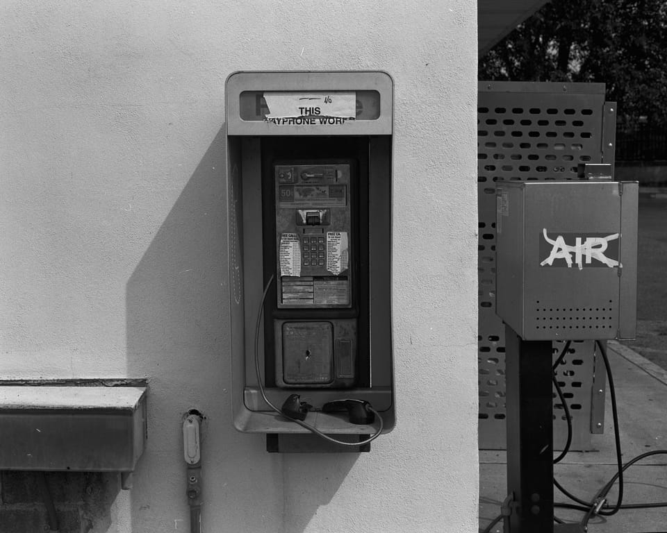 An old payphone. A worn sign on the top reads "This Payphone Works" but the broken reciever suggests otherwise.